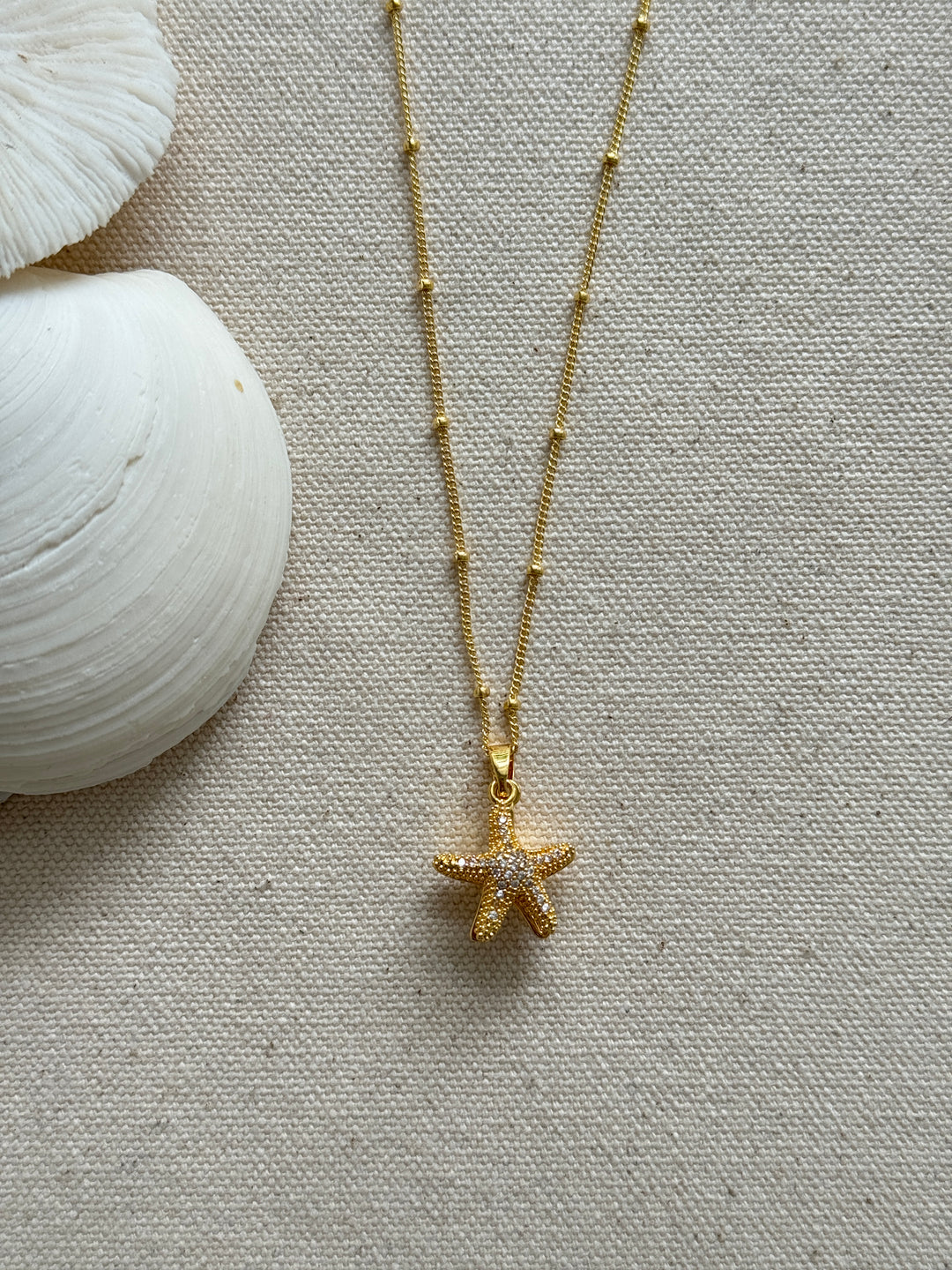 Gold necklace with a starfish pendant on a textured beige surface