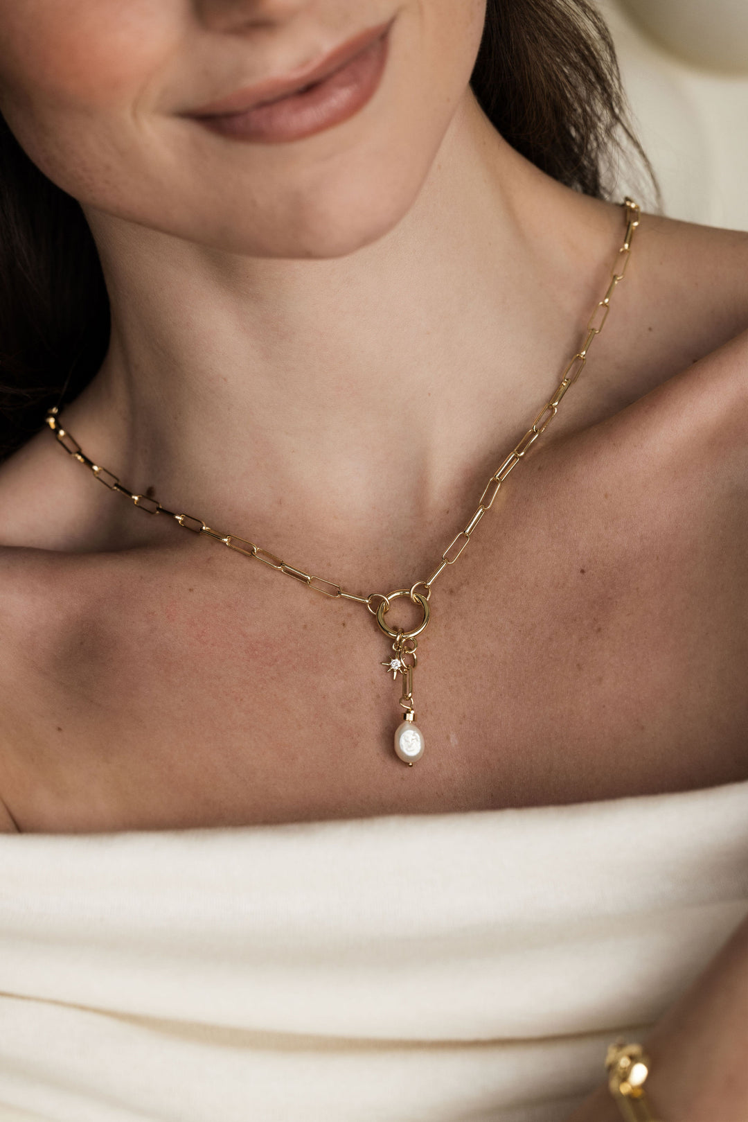 A person wearing a gold-filled chain necklace with a freshwater pearl pendant.