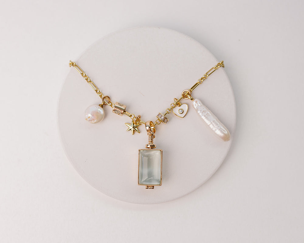 Gold necklace with a rectangle glass locket, pearl charms, star and heart charms
