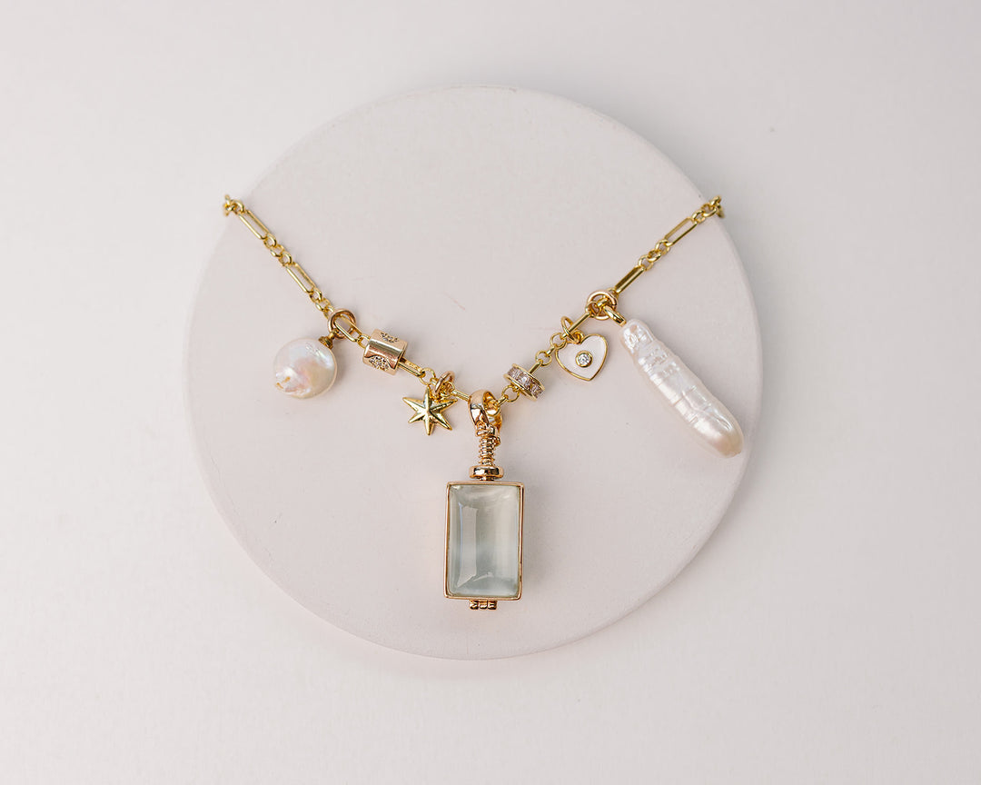 Gold necklace with a rectangle glass locket, pearl charms, star and heart charms