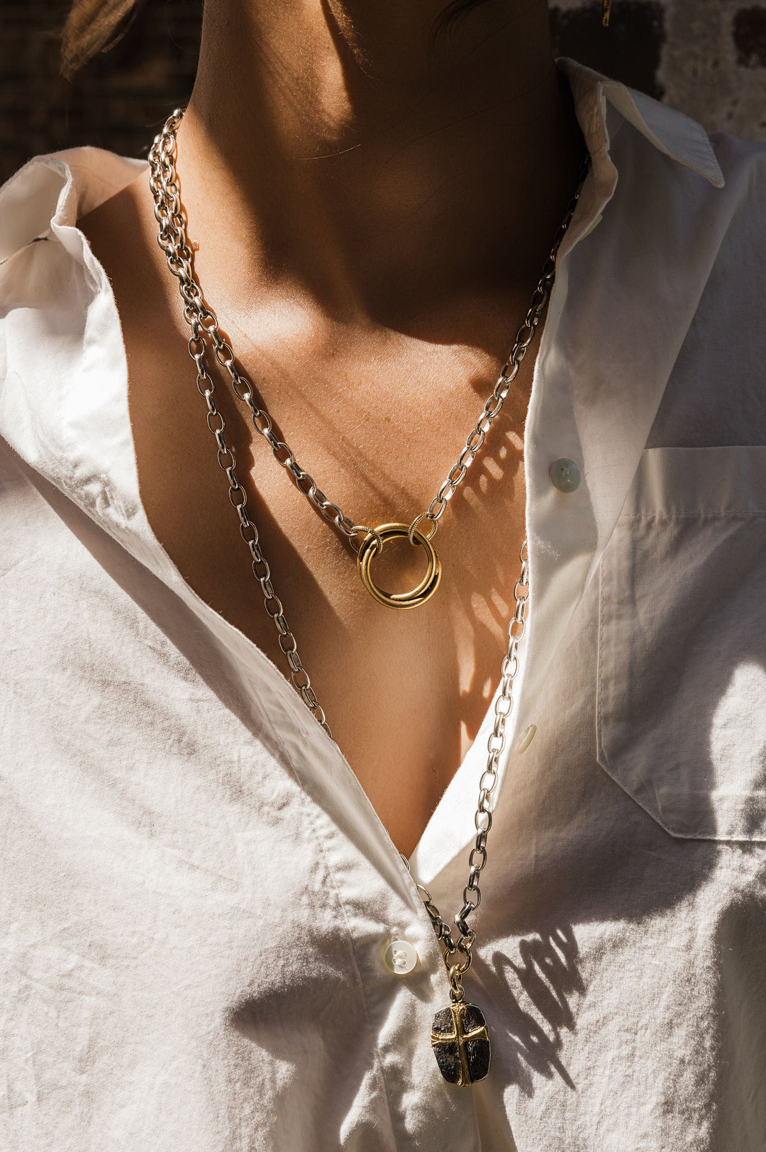 Person wearing a white shirt with a gold necklace featuring a large ring pendant.