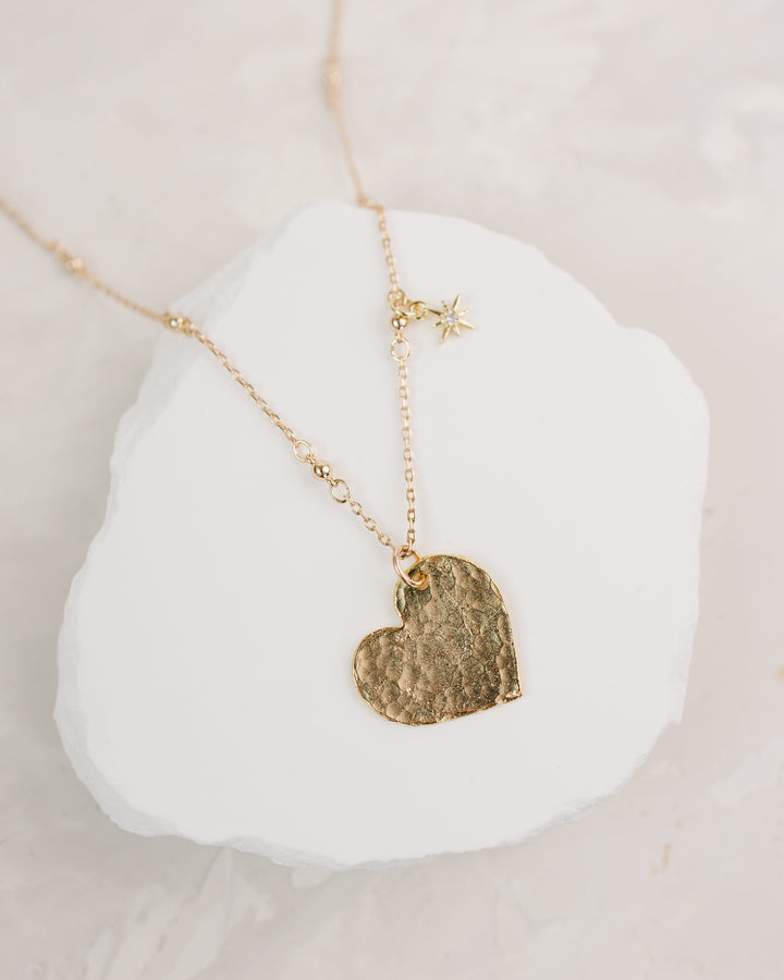 Gold necklace with a textured heart pendant on a white stone surface