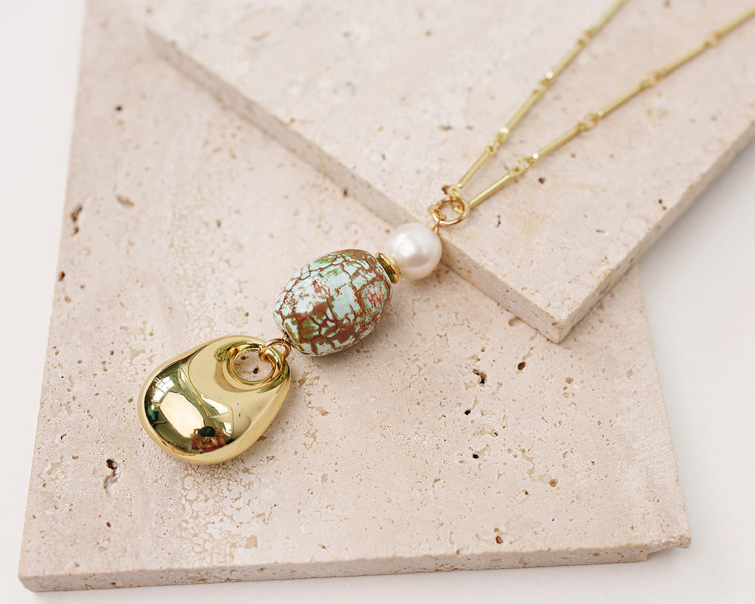 Necklace with gold pendant, marbled bead, and pearl on a beige stone surface