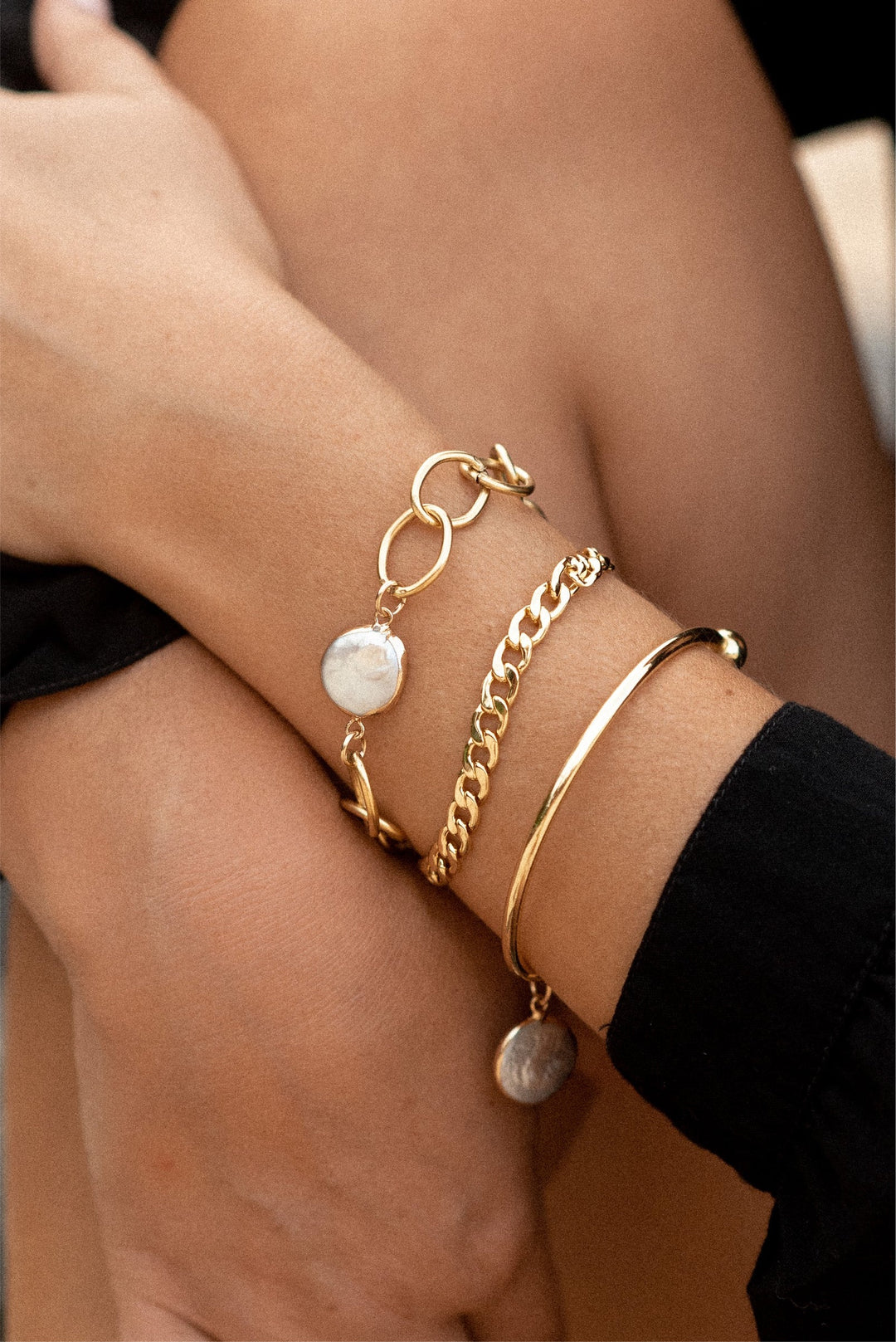 A person's wrist wearing a gold-plated chunky link chain bracelet with a central pearl and a spring closure.