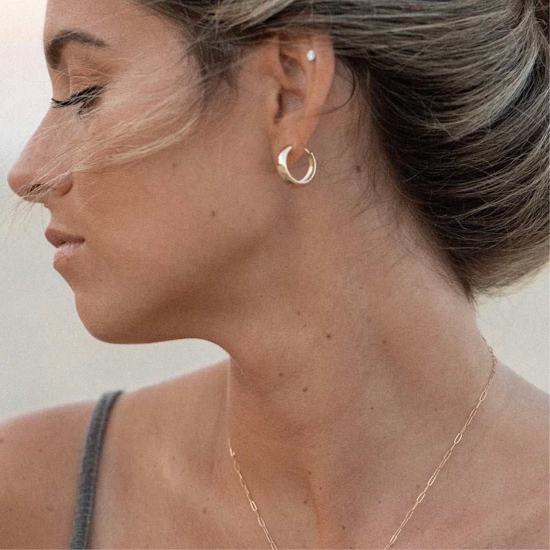 A person wearing gold hoop earrings, with the earrings visible against their ear.